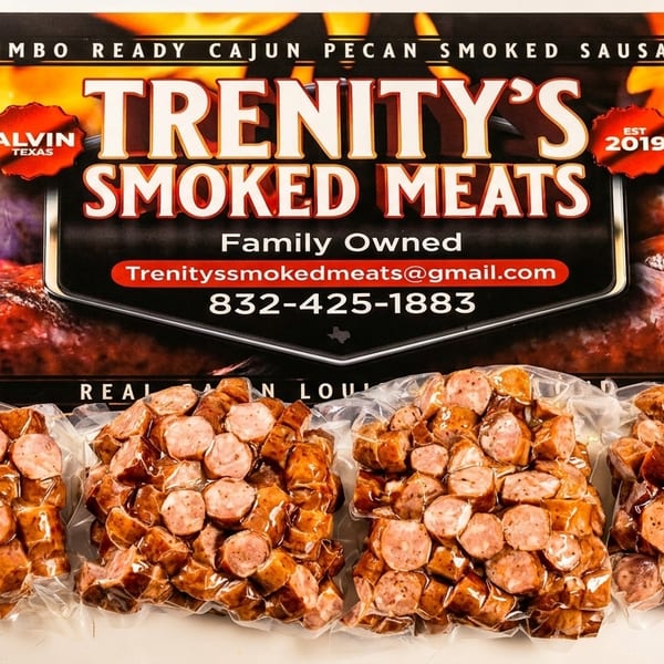 Four vacuum-sealed packages of sliced Trenity's Smoked Meats sausage in front of a brand sign.